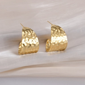 Macro detail of gold-plated geometric earrings with hammered texture on silk fabric