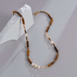 Collier en oeil de tigre avec perles et accents dorés sur un fond de pierre minimaliste
