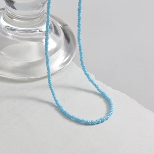 Close-up of minimalist light blue seed bead necklace layered on a white card display
