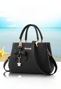 Detail of black pebbled leather handbag with bow charm and gold hardware on beach background