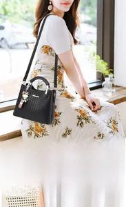Detail der schwarzen Handtasche mit Webstruktur, Schultergurt und süßem Kuh-Anhänger