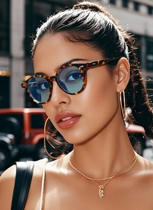 Close-up of tortoise shell sunglasses with blue lenses and gold jewelry on model