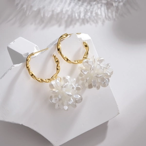 Detailansicht goldener gedrehter Ohrringe mit eleganten weißen Blumen-Anhängern