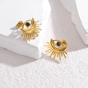 Boucles d'oreilles œil porte-bonheur dorées avec pierre noire sur socle blanc