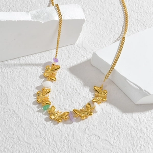 Collier papillon doré avec pierres colorées disposé sur des blocs de marbre blanc