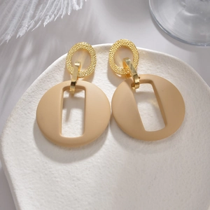Minimalistische goldene Metall- und beige Harzohrringe mit Hohlkreis auf weißem Teller