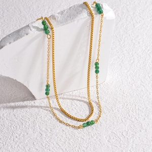 Detailed shot of double-layered gold chains with vibrant green beads on white stone