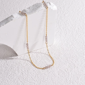 Close-up of gold chain necklace with light purple beads on a textured white rock base