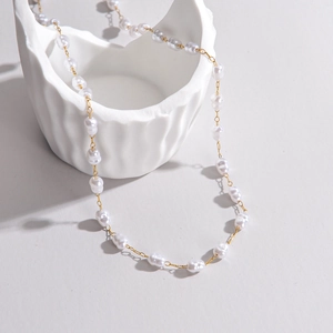 Close-up of Baroque freshwater pearl necklace with gold chain on artistic white ceramic