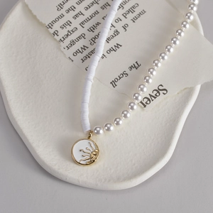 Collana alla moda con perle, dischi bianchi e ciondolo a sole dorato su piatto in ceramica