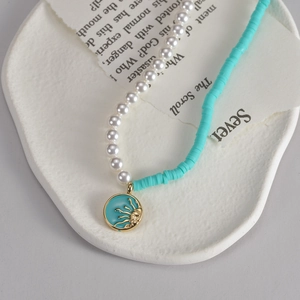 Collana bohémien con perle e perline heishi blu e ciondolo a sole dorato su piatto bianco