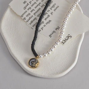 Dettaglio della collana asimmetrica con perle, grani neri e medaglione con sole