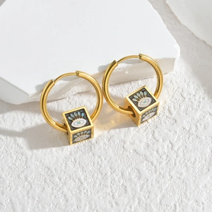 Gold cube earrings with enamel evil eye charms on minimalist textured white background