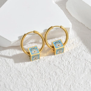 Detail of gold hoop earrings with blue cube charms featuring evil eye patterns