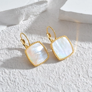 Détail de boucles d'oreilles dorées carrées avec nacre irisée et bordure perlée chic