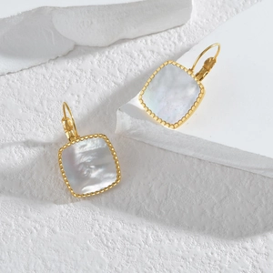 Détail de boucles d'oreilles carrées dorées en nacre avec bord perlé sur pierre blanche