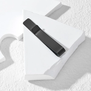 Minimalist matte black stainless steel tie clip displayed on geometric white stone blocks