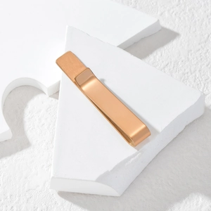 Minimalist rose gold tie clip with brushed metal texture on white geometric block