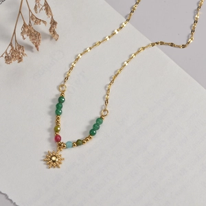 French design gold sun pendant necklace with colorful beads on a white textured background