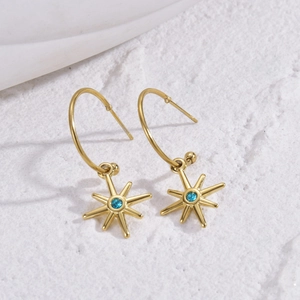 Elegant gold eight-pointed star earrings with a bright blue stone on a white stone background