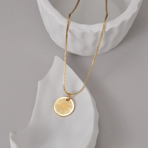 Gros plan détaillé du pendentif soleil en acier doré 14K et de sa maille plate serrée