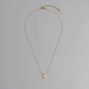 Gros plan du collier doré en acier inoxydable avec petit pendentif tête de mort et fermoir