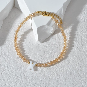 Detail van champagne kralenarmband met witte X-hanger en goudkleurige karabijnsluiting