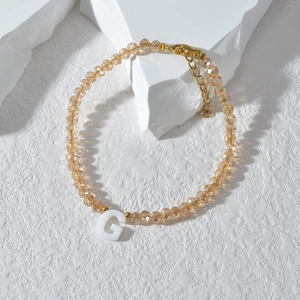 Detail van kralenarmband met G-letter hanger en gouden metalen karabijnsluiting