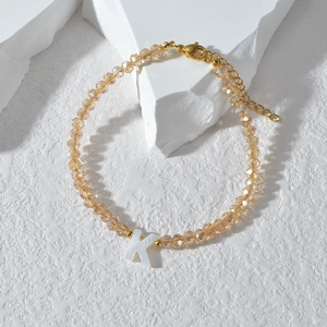 Detailopname van een kralenarmband met 'K'-bedel en een gouden karabijnsluiting