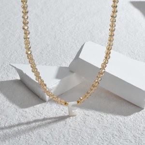 Vue détaillée du collier en perles champagne avec un pendentif blanc en forme de lettre E