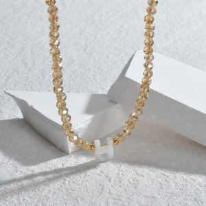 Détail d'un collier en perles de cristal champagne avec un pendentif lettre H blanc