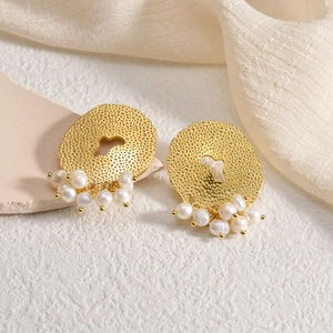 Elegant gold hammered metal oval earrings with dangling white pearls on stone surface