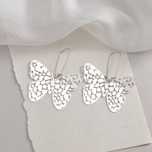 Minimalist silver butterfly cutout drop earrings with long hooks on artistic white fabric