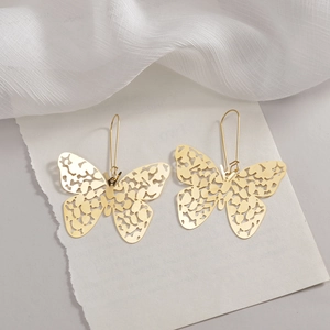 Elegant gold-tone hollow butterfly pendant earrings displayed on white textured paper