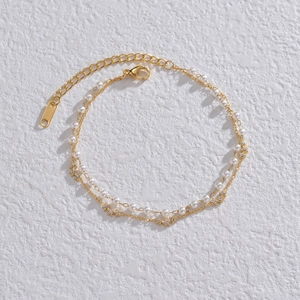 Double-layered gold chain bracelet with pearls and star pendants on white background