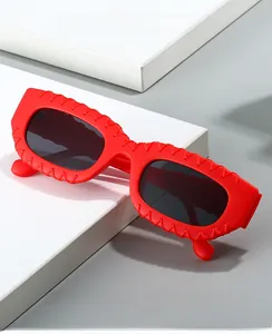 Détail de lunettes de soleil carrées rouges avec texture tissée sur la monture et verres gris