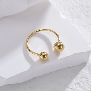 Gold horseshoe U-shaped open ring with polished ball ends on textured stone background