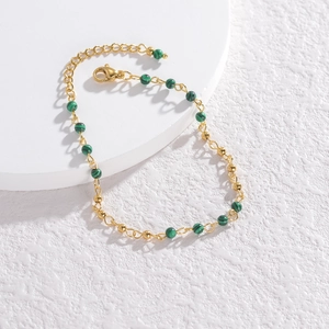 Minimalist gold beaded bracelet with green malachite stones on a white display stand