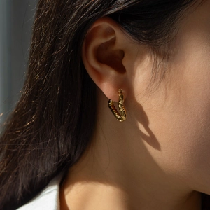 Détail de boucles d'oreilles créoles dorées texturées portées par un mannequin femme
