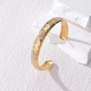 Gold stainless steel open bangle with embossed star patterns and pave crystals on white stone