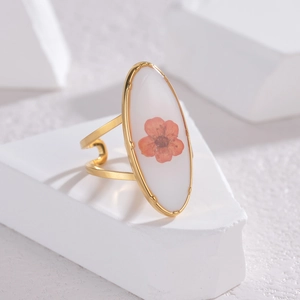 Détail macro de la bague ovale dorée avec véritable fleur séchée orange et base résine