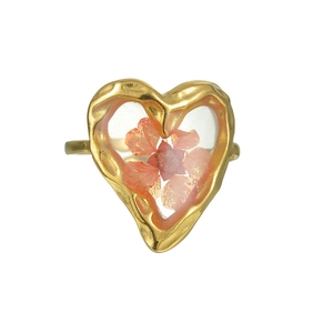 Détail d'une bague en forme de cœur avec fleur séchée orange et cadre doré martelé