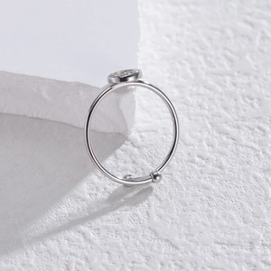 Minimalist silver open ring with circular zircon inlay on white textured stone background