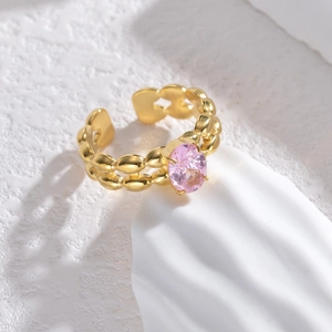 Anello dorato regolabile con gemma rosa ovale e texture a spiga su sfondo di pietra bianca