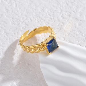 Macro dell'anello dorato intrecciato con pietra blu quadrata e gambo regolabile