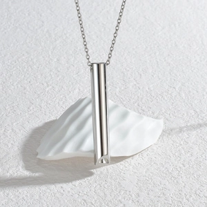 Polished silver cylindrical whistle pendant necklace on minimalist white display stand