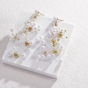 Detail view of long tassel earrings with white pearls and gold beads on a stone display