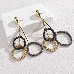 Detailed view of gold drop earrings featuring geometric beaded tassel rings on white stone
