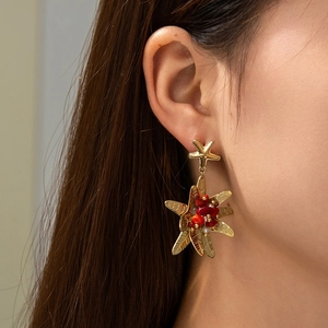 Detailed view of starfish stud earrings with red beads and golden leaf tassels worn on ear