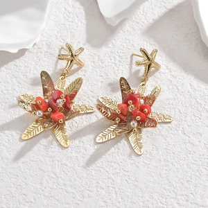 Detailed close-up of gold starfish earrings with red coral and white pearl accents